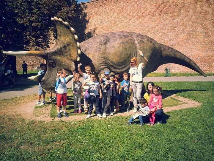 Deca sa vaspitačem ispred modela dinosaurusa na letnjem izletu