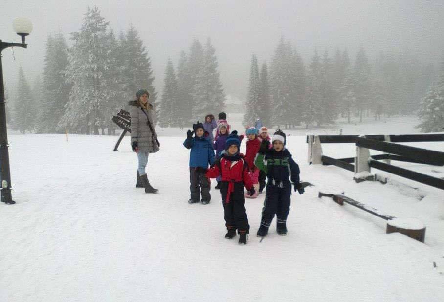 Deca sa vaspitačem u zimskoj šetnji kroz sneg, pored zavejane šume